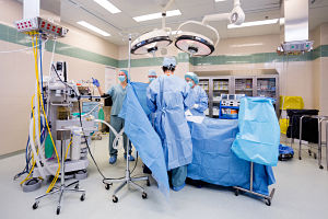 A group of doctors wearing blue masks and blue scrubs gathered around an operating table surrounded by medical equipment