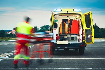 A blurred medical professional quickly pushing a gurney to the open back doors of a bright yellow ambulance