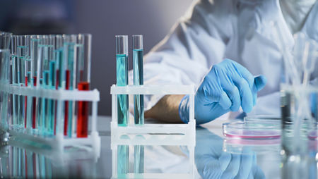 A rack of test tubes filled with red and blue liquid with the gloved hand and of a doctor in the background