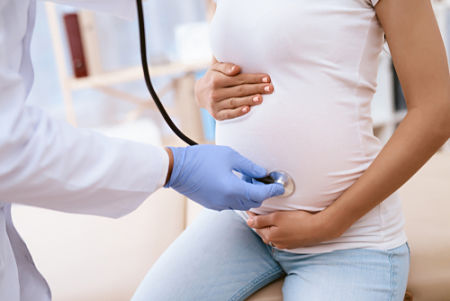 A medical professional wearing gloves and holding a stethoscope to the stomach of a pregnant woman