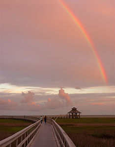 A rainbow in the clouds over two people walking down a long walkway